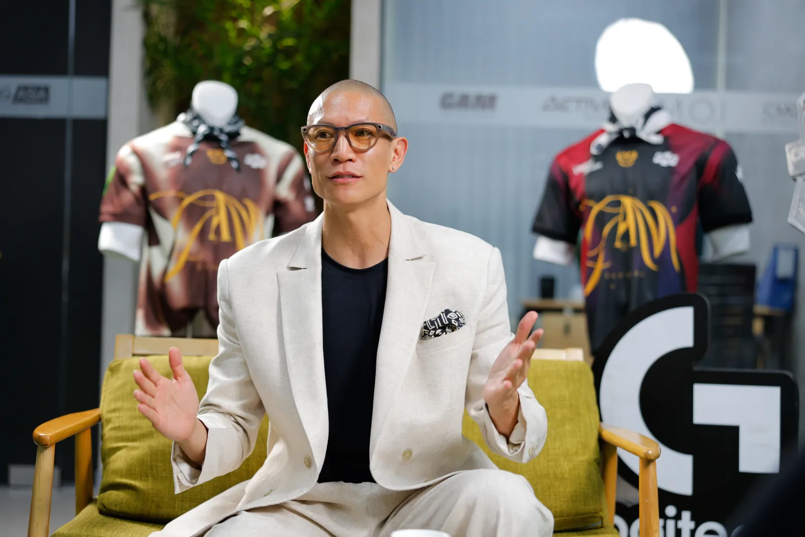 TK Nguyen in a cream suit on a Logitech shoot at the GAM office, GAM jerseys behind him
