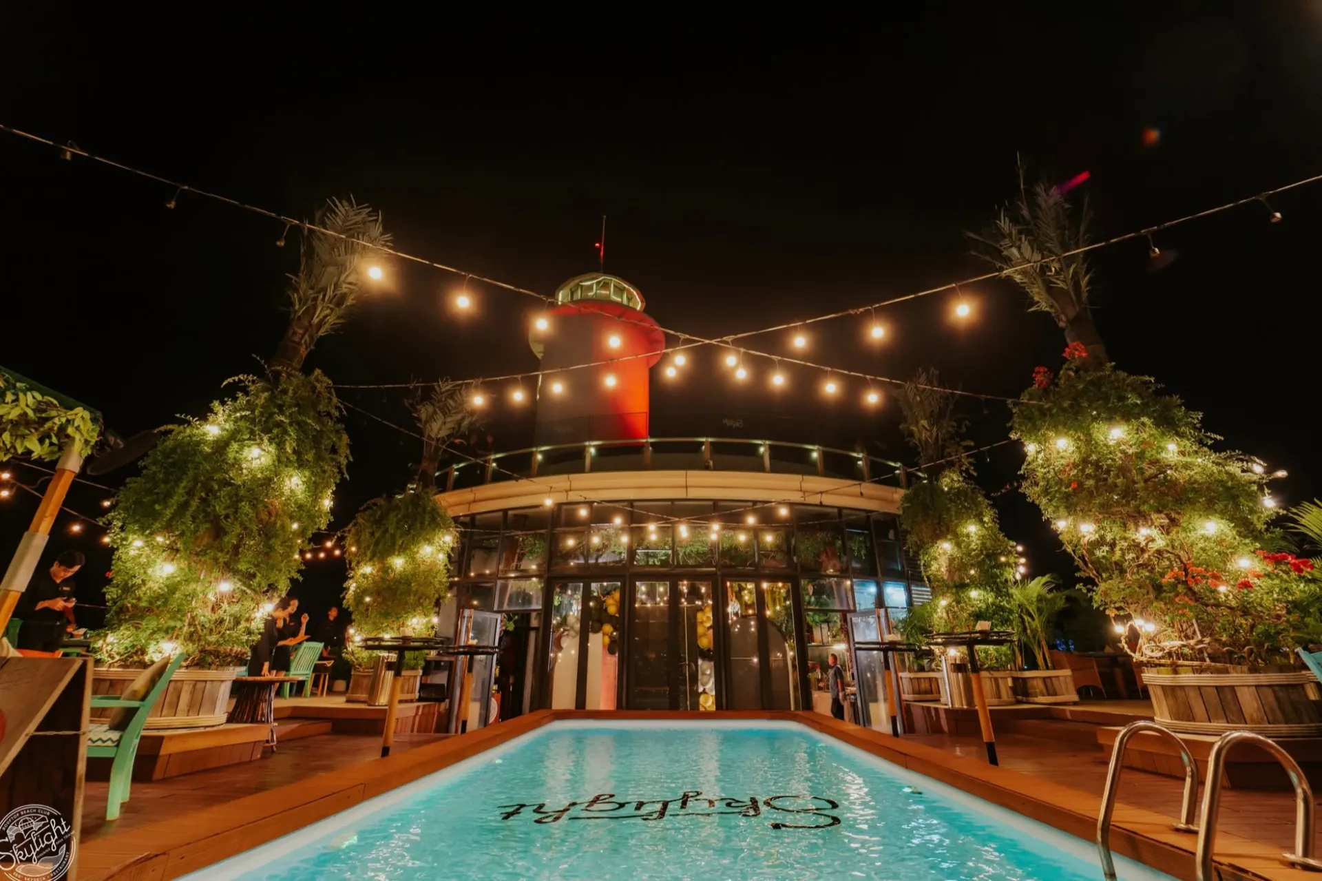 The Skylight pool at night under string lights, the red lighthouse behind