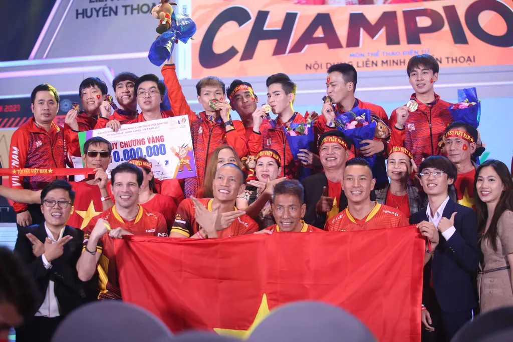 Team Vietnam's League of Legends squad celebrating SEA Games 31 gold on stage with the Vietnamese flag and confetti, 2022