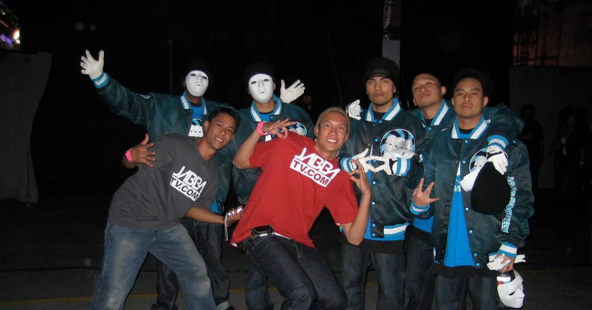TK Nguyen in a red JabbaTV shirt with the masked Jabbawockeez on finale night of America's Best Dance Crew