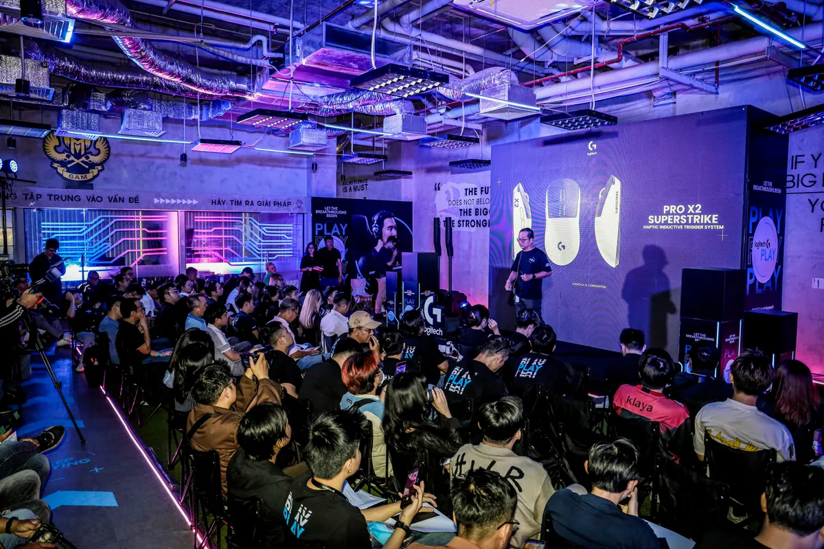 A packed room at Logitech G PLAY 2025 inside the GAM office, the GAM crest on the wall and the PRO X2 SUPERSTRIKE on the big screen, a fan in a Kiaya jersey in the crowd